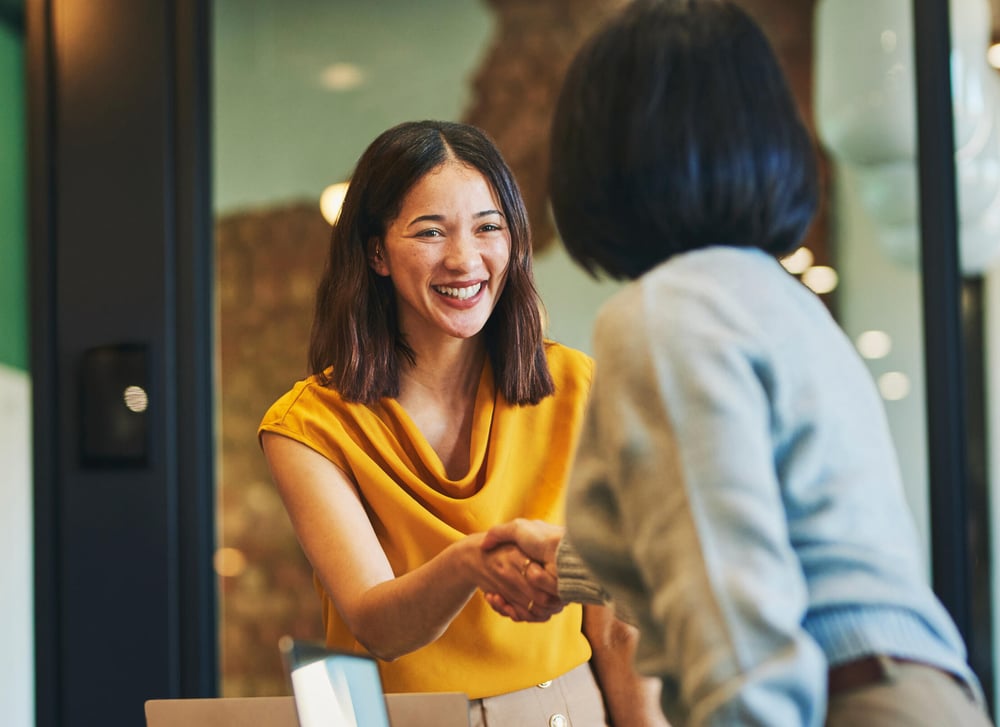 Two women smile and shake hands